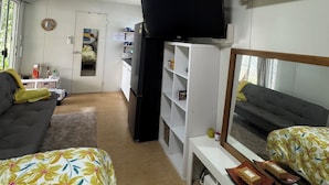 Ett litet rum med en soffa, en säng med blommigt sänglinne, en tv som är monterad på väggen och en luftkonditioneringsanläggning.