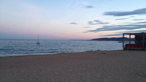 A beach with a small boat in the water, a lifeguard tower, and a distant shoreline. - APARTMENT T3 - Private parking - 300 m SEA & BEACH (Fréjus)