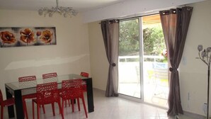 A dining area with a glass table and red chairs, a chandelier, and a sliding glass door to the outside. - APARTMENT T3 - Private parking - 300 m SEA & BEACH (Fréjus)