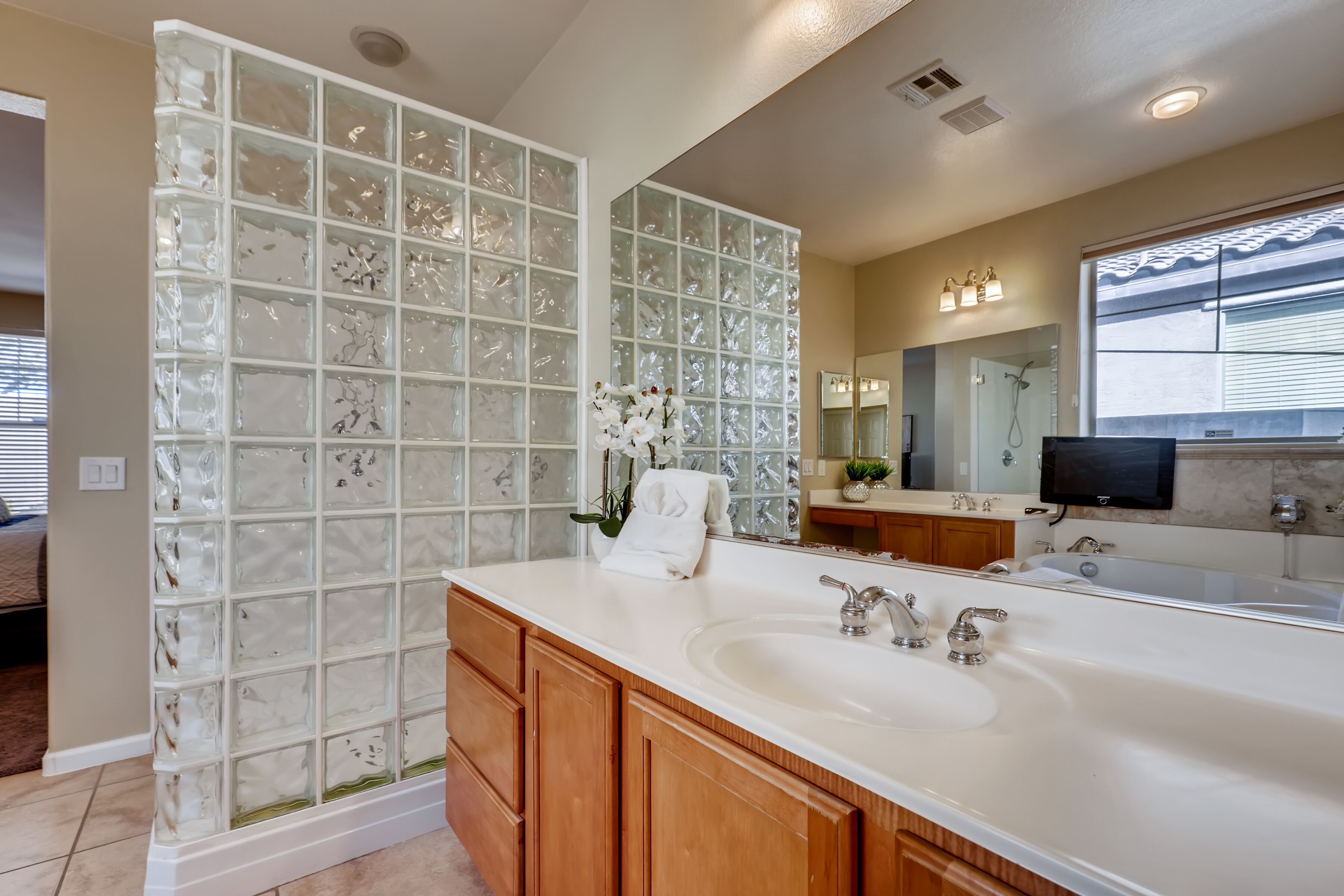 Une salle de bain moderne dotée d’une grande douche à parois de verre, d’un meuble-lavabo double avec un évier et un miroir, et d’un téléviseur fixé au-dessus du miroir.