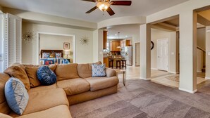A living room with a sectional sofa, a ceiling fan, and a view into the kitchen and dining area. - Vegas Themed 6BR · Game Room · 2 Suites · EV  · Spacious Retreat For 14 Guest (North Las Vegas)