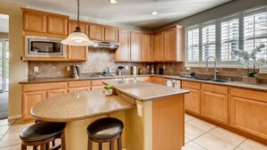 A kitchen with wooden cabinets, a granite countertop, a built-in microwave, a stainless steel range hood, and a window with blinds. - Vegas Themed 6BR · Game Room · 2 Suites · EV  · Spacious Retreat For 14 Guest (North Las Vegas)