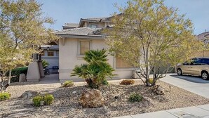A residential house with a sloped roof, a front porch, and a landscaped garden with rocks and small trees. - Vegas Themed 6BR · Game Room · 2 Suites · EV  · Spacious Retreat For 14 Guest (North Las Vegas)