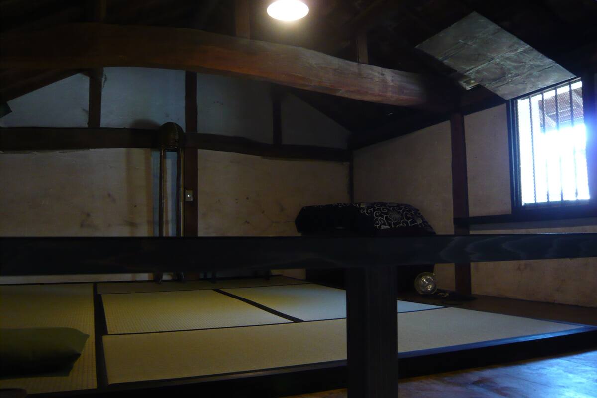 A traditional tatami mat room with a low ceiling and wooden beams.