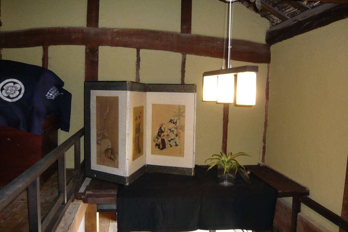 A traditional Japanese room with tatami flooring, a shoji screen, a black table with a lamp, and a wooden bench.