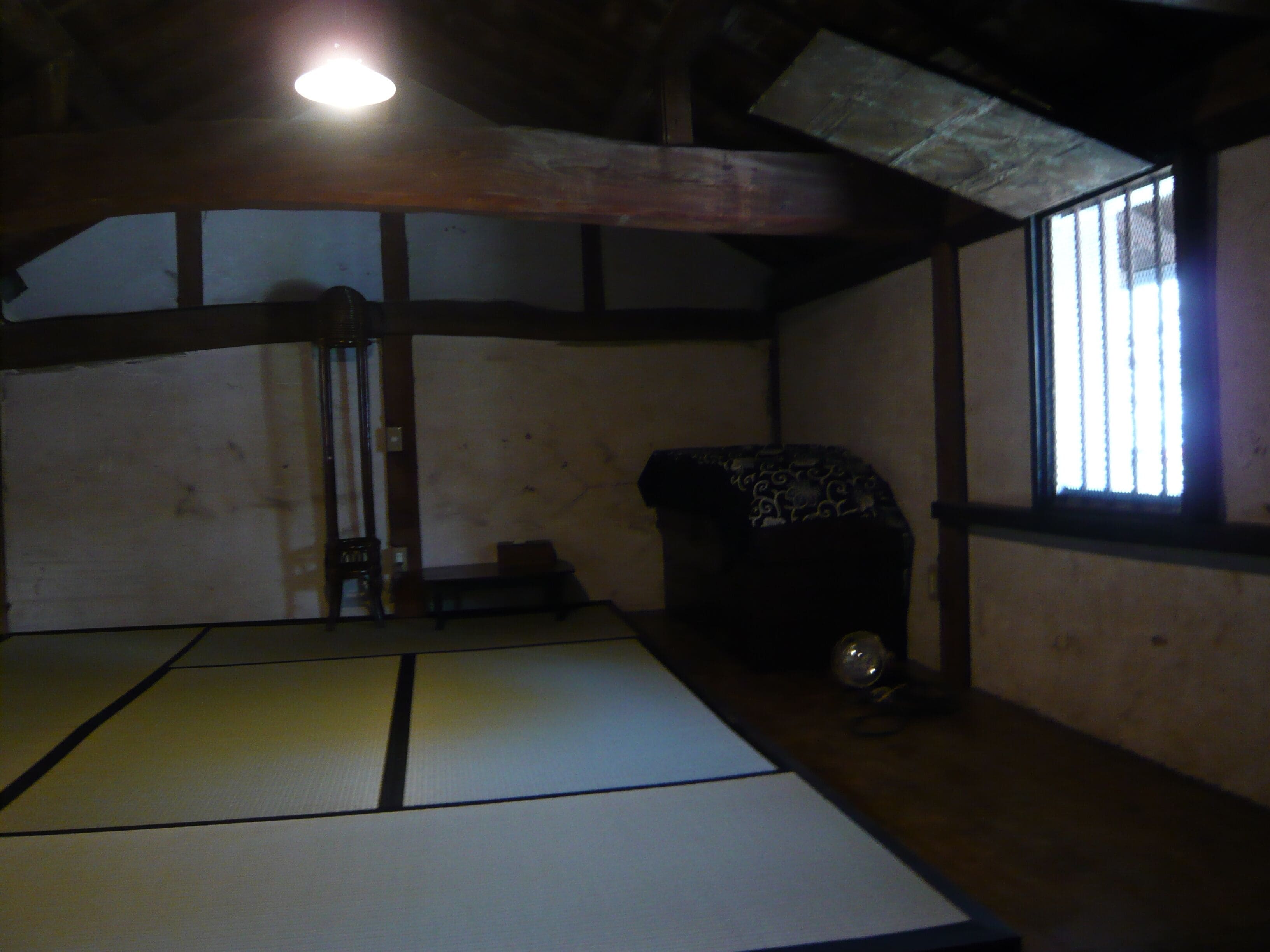 A tatami mat room with a low ceiling, wooden beams, and a window with bars.