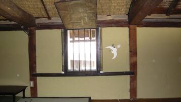 A room with a traditional wooden ceiling, a window with a bamboo blind, and a wall with a white bird mural.