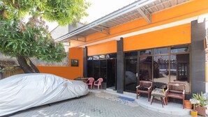 Une voiture garée sous un abri devant un bâtiment aux murs orange, doté de grandes fenêtres et d’une terrasse.