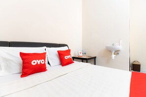 Ein Hotelzimmer mit einem Bett, zwei rote Kissen mit dem Schriftzug "OYO", einem weißen Waschbecken und einem kleinen Tisch mit Toilettenartikeln.
