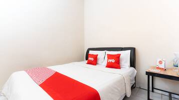 A hotel room with a bed, two red pillows, a white bedspread, and a small table with a water bottle and a menu.