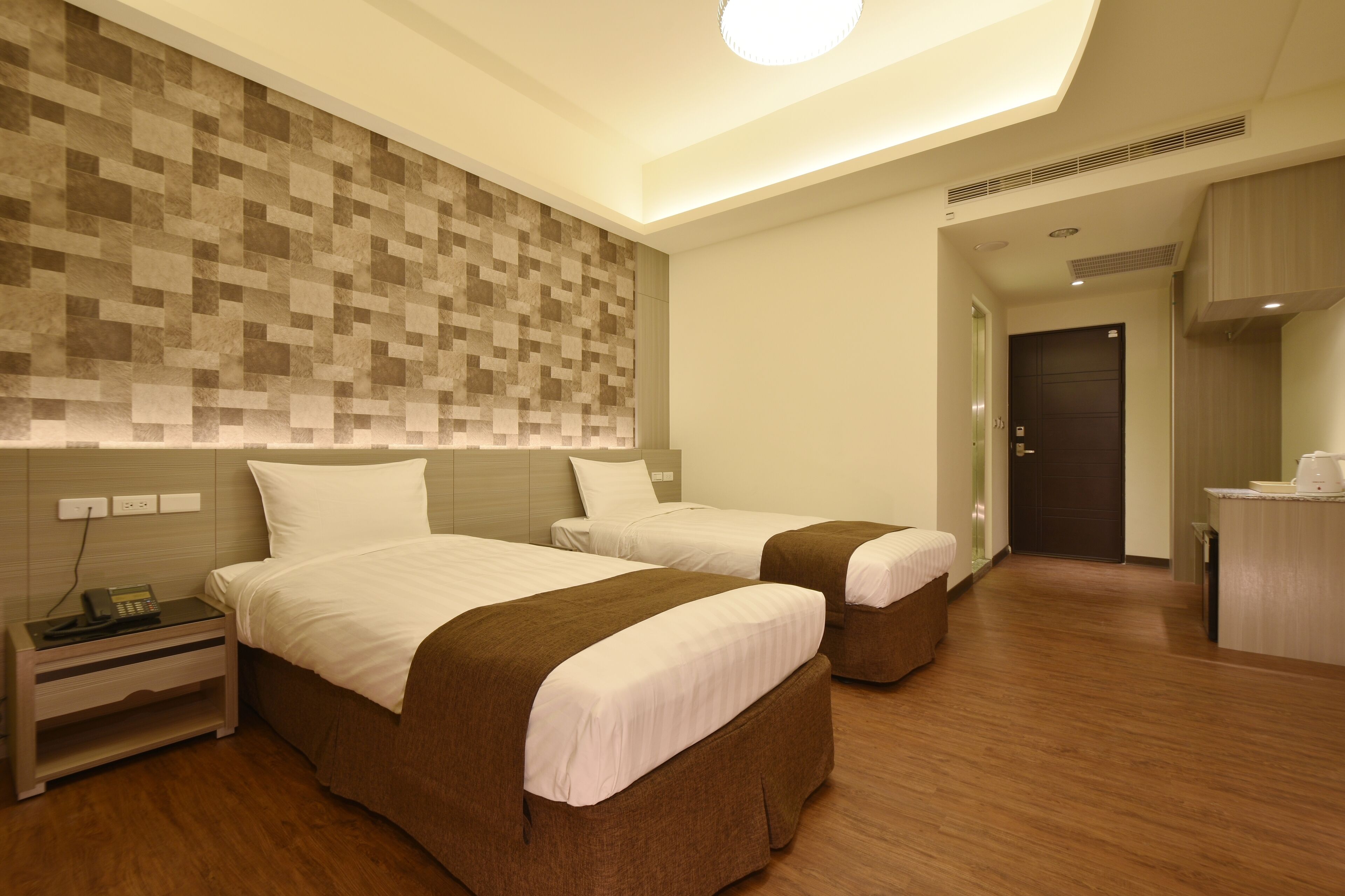 A hotel room with two beds, a nightstand with a phone, a wall with a pixelated pattern, and a door leading to another room.