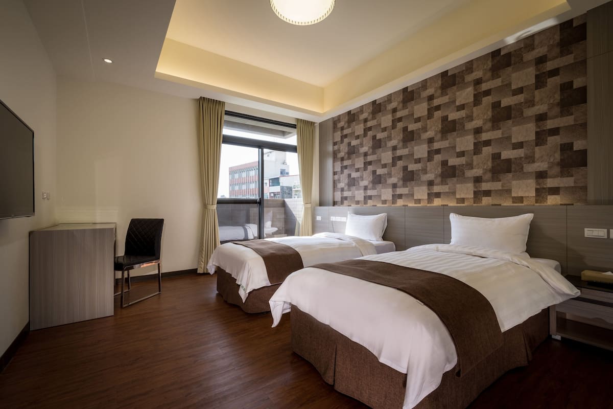 A hotel room with two beds, a desk, and a chair.