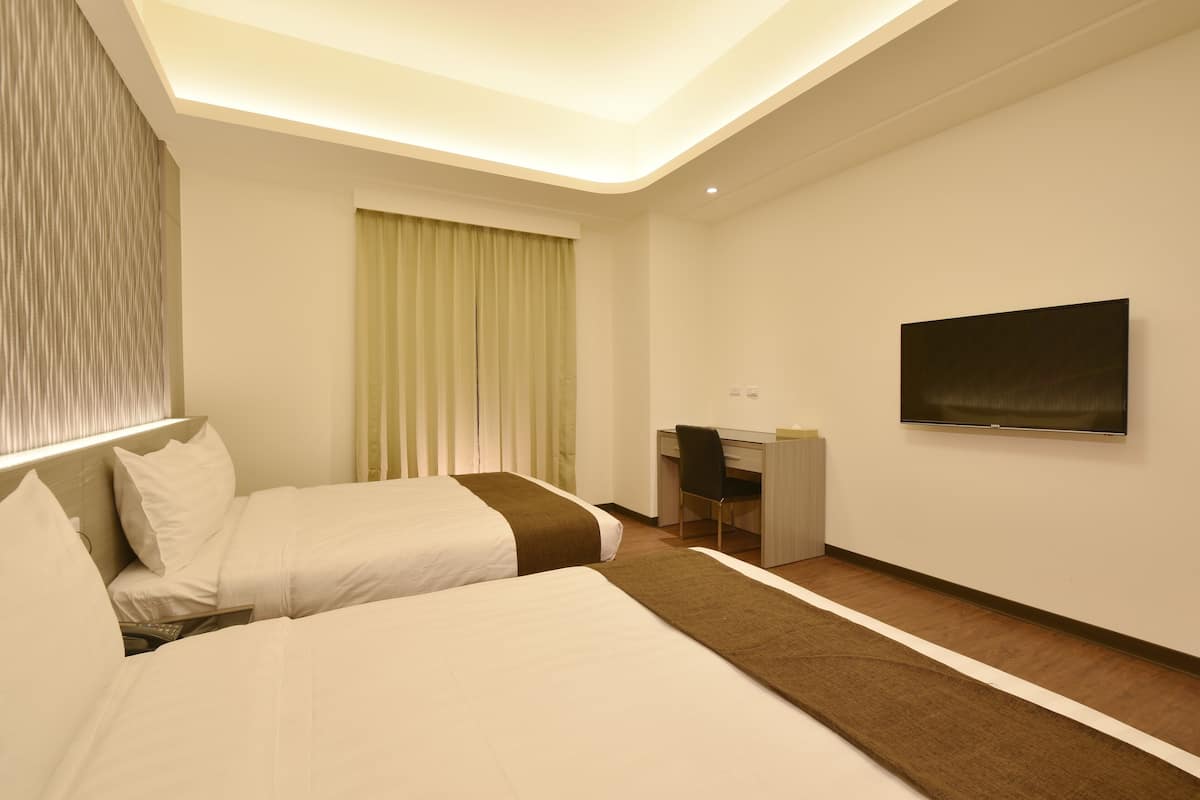 A hotel room with two beds, a desk, a chair, a television, and a window with curtains.