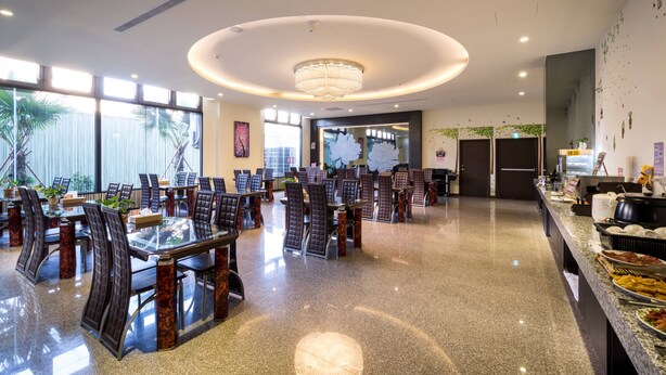 Un amplio comedor con mesas y sillas redondas, una araña y un mostrador de buffet con diversas opciones de comida.