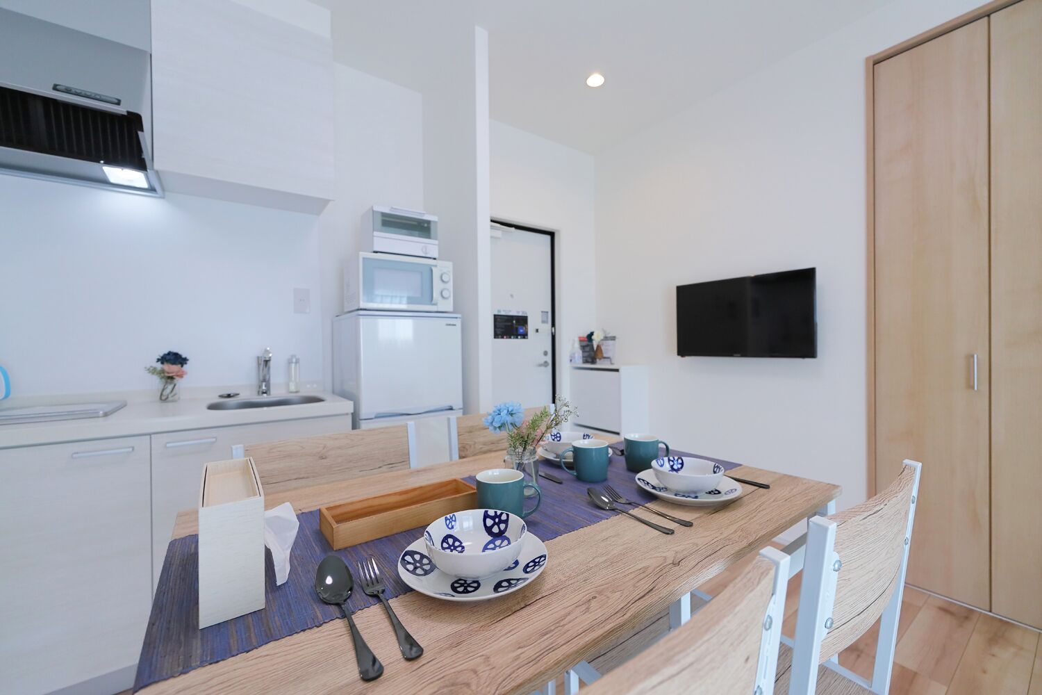 Una cocina moderna con electrodomésticos blancos, una mesa de comedor con platos azules y blancos, y un televisor montado en la pared.