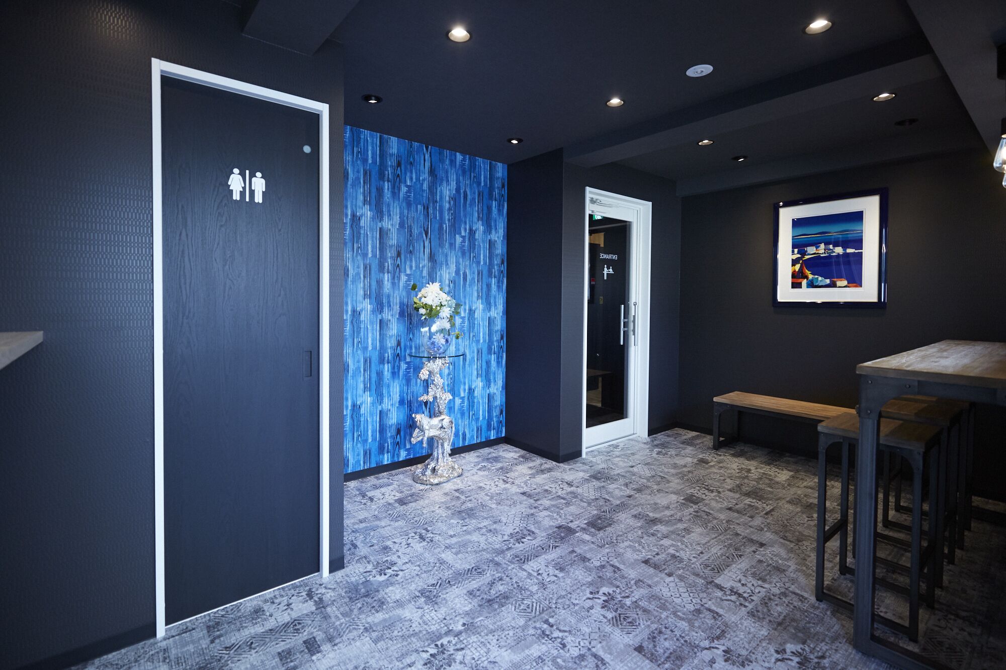 A hallway with a blue textured wall, a door with a white frame, a bench, and a framed picture on the wall.