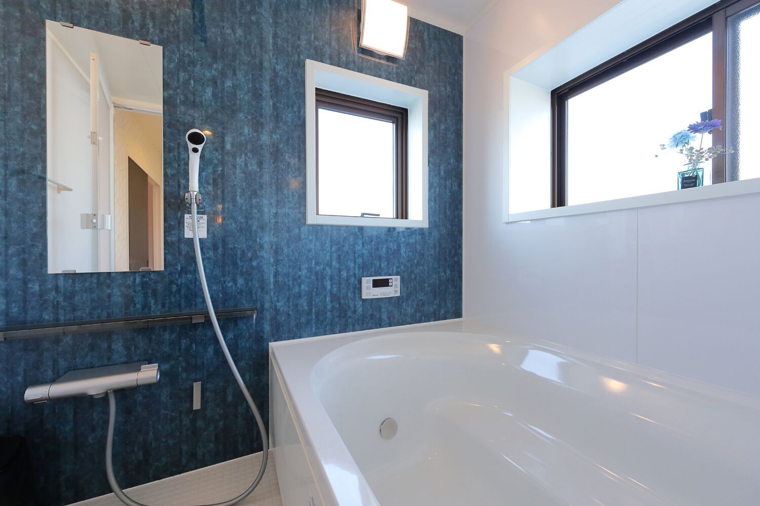 Une salle de bain moderne dotée d’une grande baignoire, d’une douchette et d’une fenêtre laissant entrer la lumière naturelle.
