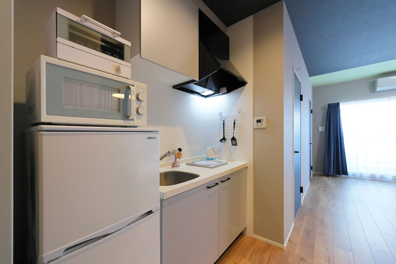 A compact kitchen with a refrigerator, microwave, and stove, a sink with a faucet, and a window providing natural light.