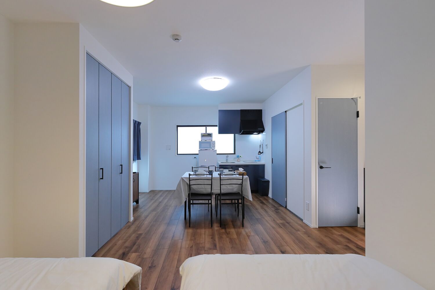 A compact room with a bed, a small dining table with chairs, a kitchenette, and a window.