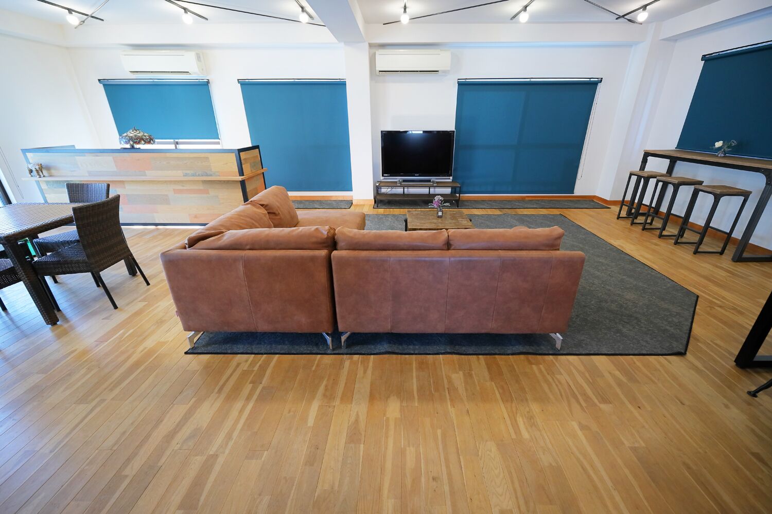 Una sala de estar moderna con un sofá marrón, suelo de madera, un televisor y una zona de comedor con sillas y una mesa.