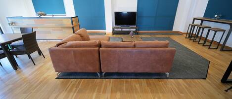 Una sala de estar moderna con un sofá marrón, suelo de madera, un televisor y una zona de comedor con sillas y una mesa.