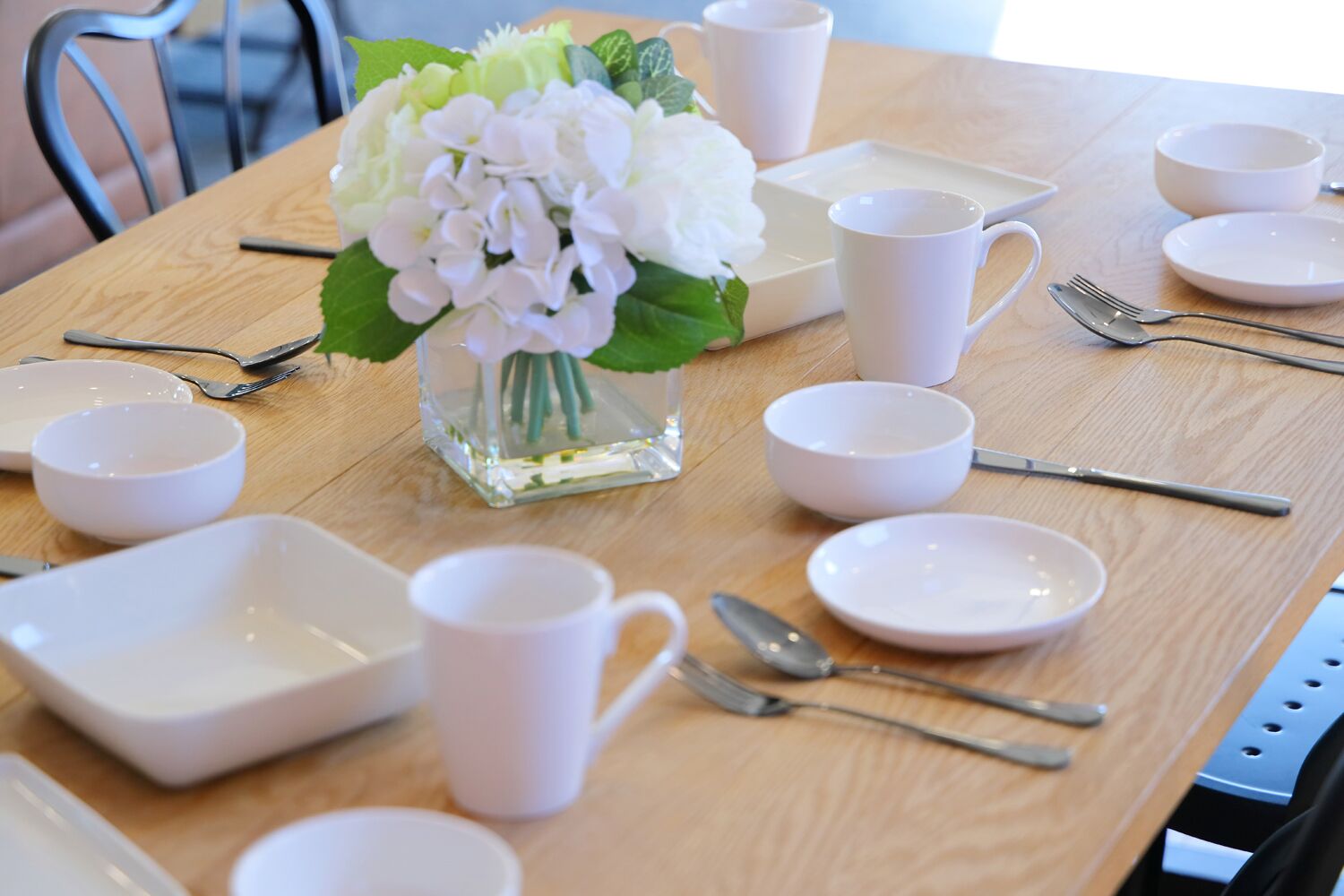 A dining table set with white dishes, cups, and cutlery.