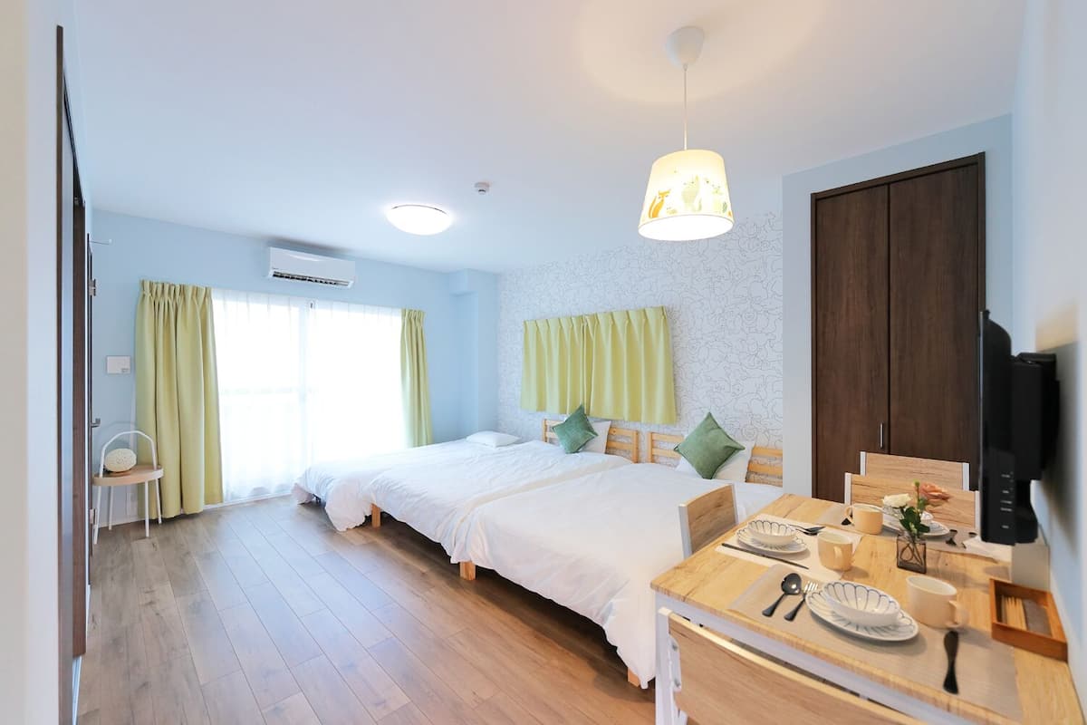 Une chambre avec deux lits, une table à manger avec des aliments pour le petit-déjeuner, une télévision et une fenêtre avec des rideaux.