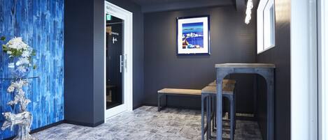 A hallway with a blue textured wall, a framed picture, a bench, and a door with an exit sign.