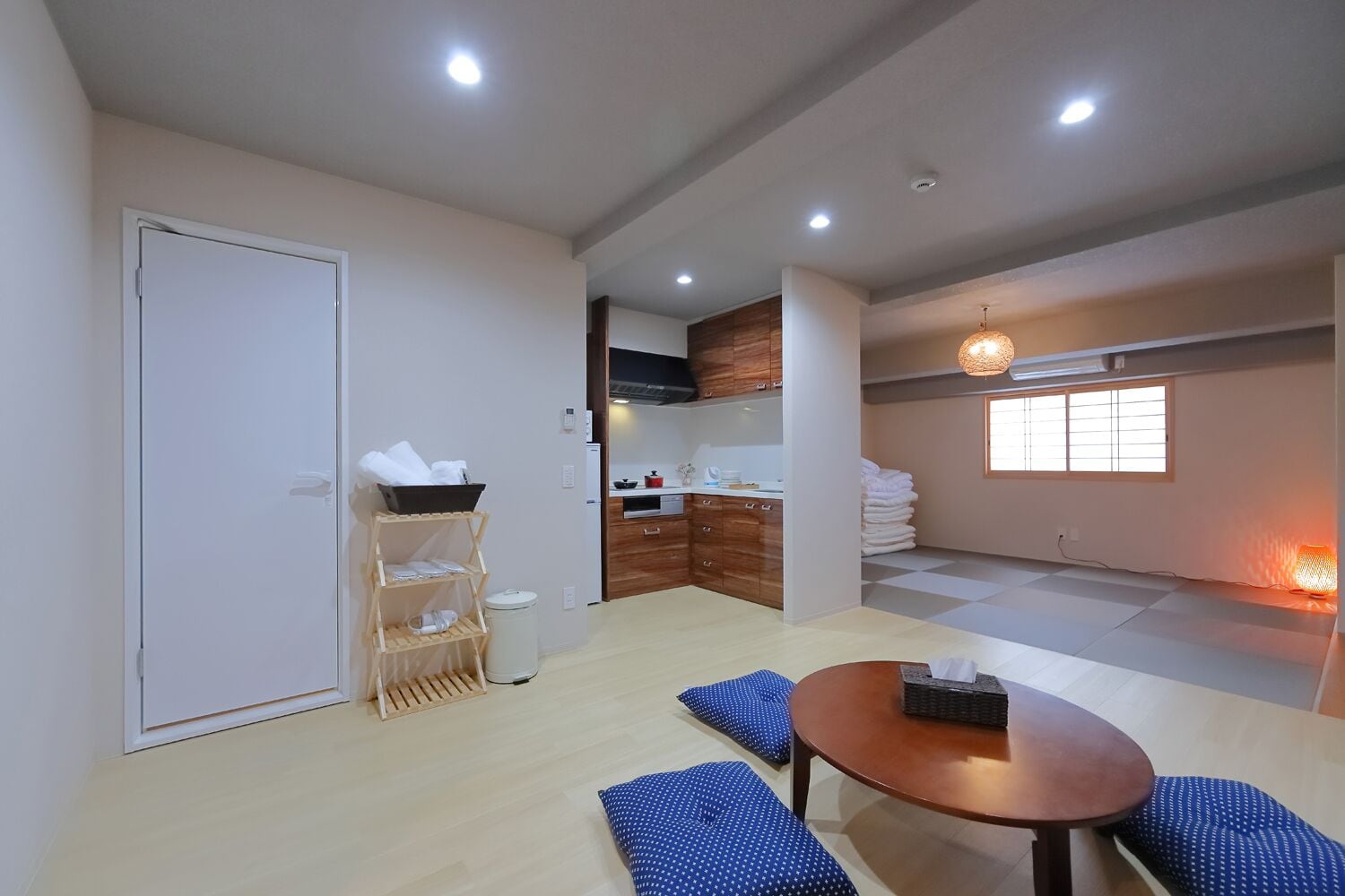 Espaço compacto para viver, com cozinha compacta, área de refeições com mesa e almofadas azuis, guarda-roupa e janela com vista.