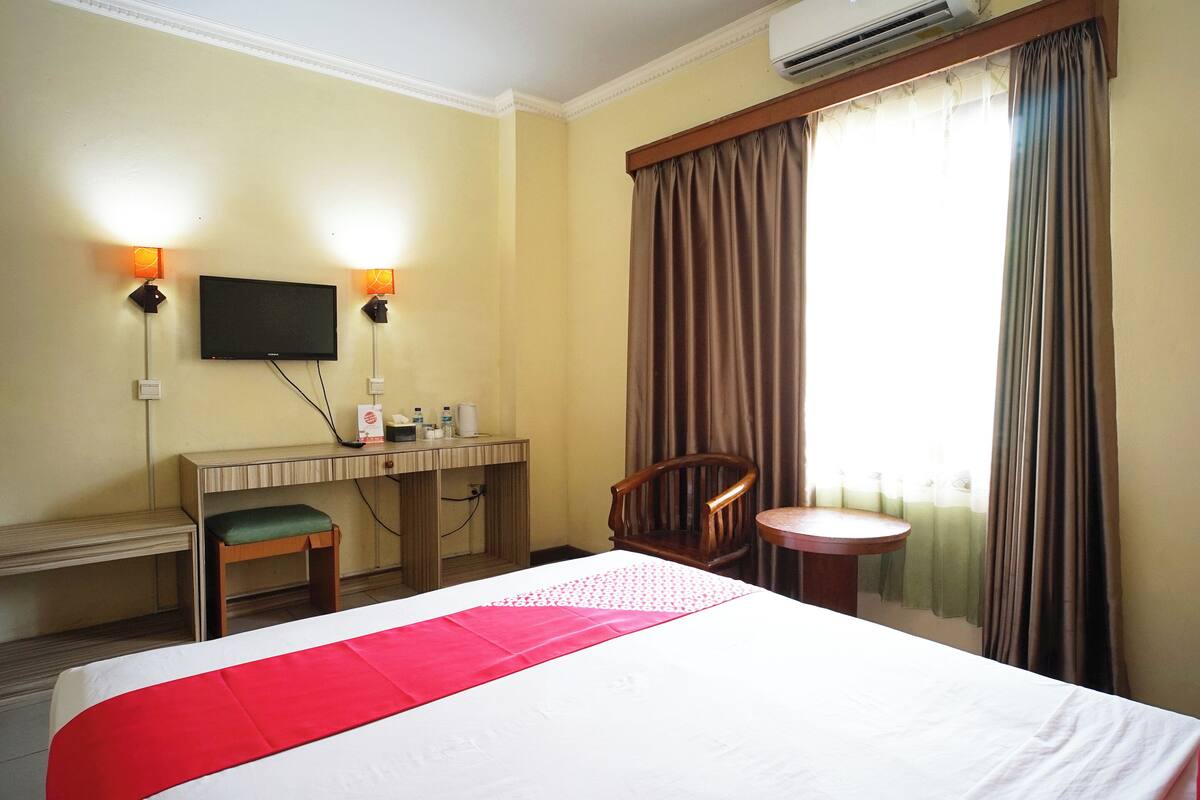 A hotel room with a bed, desk, chair, and a TV mounted on the wall.