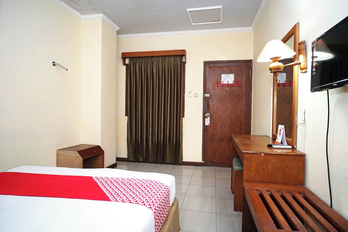 A hotel room with a bed, a desk, a mirror, a television, and a door.