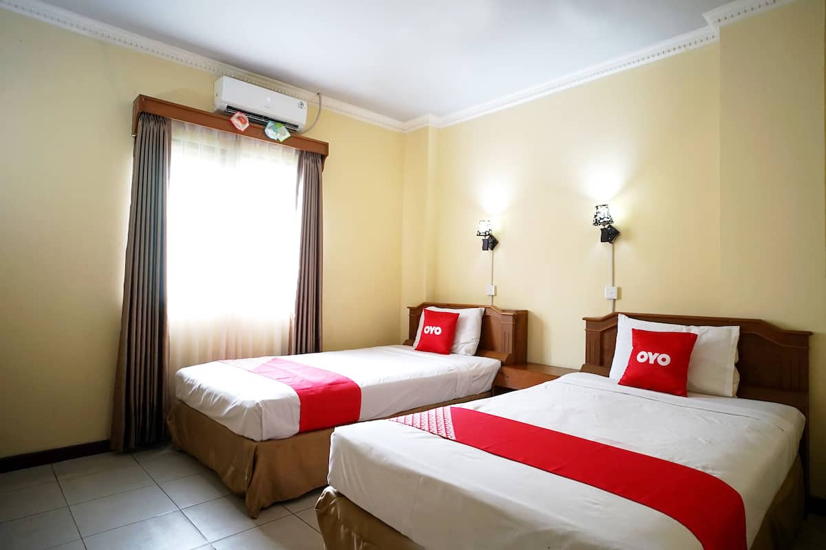 A hotel room with two beds, beige walls, a window with curtains, an air conditioner, and a night light.