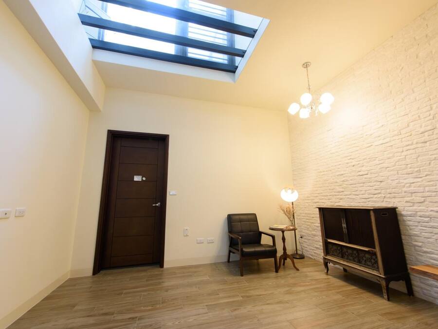 A room with a skylight, a door, a chair, a small table with a lamp, and a cabinet.