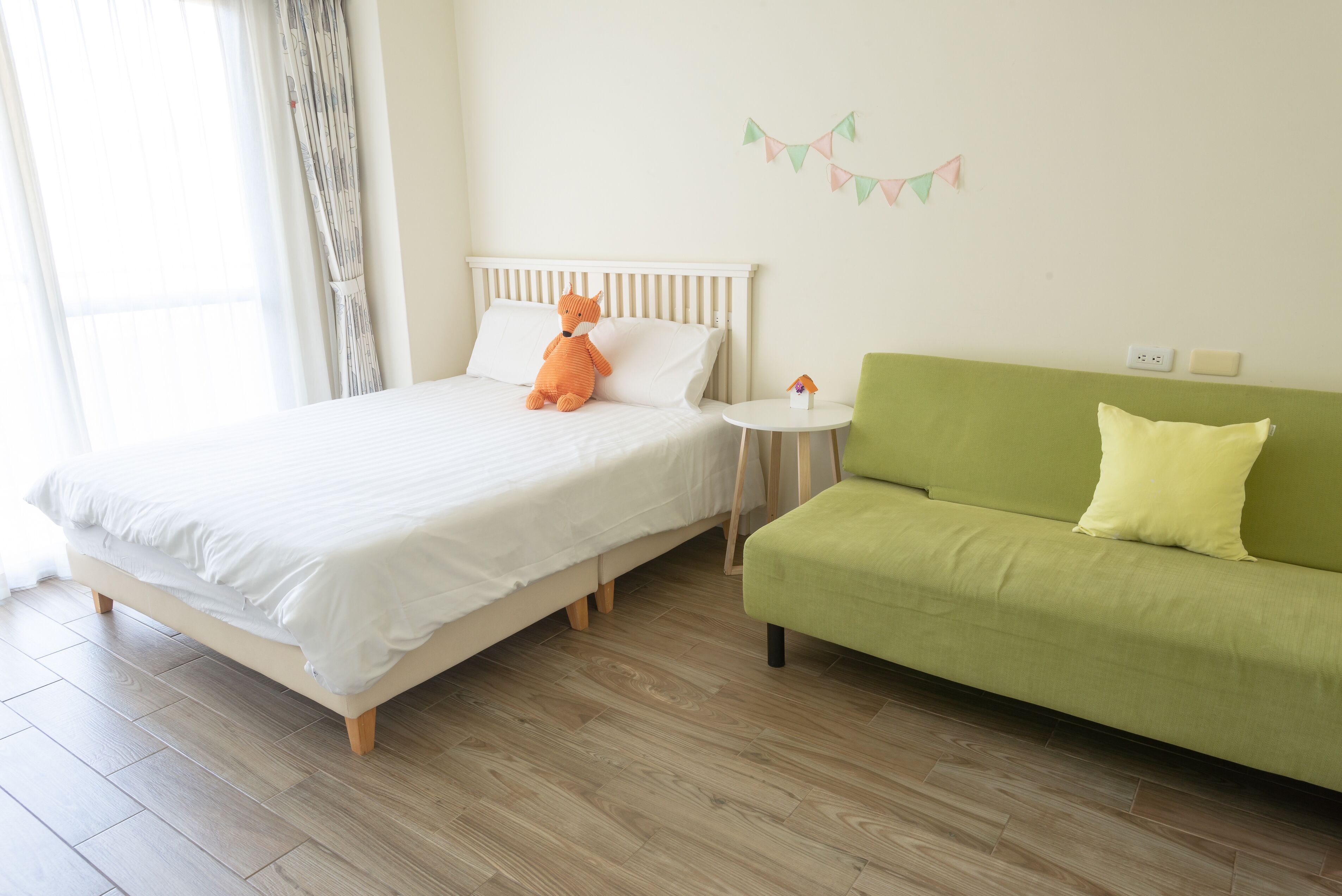 A bedroom with a bed, a green sofa, a small round table, and a wall-mounted decoration.