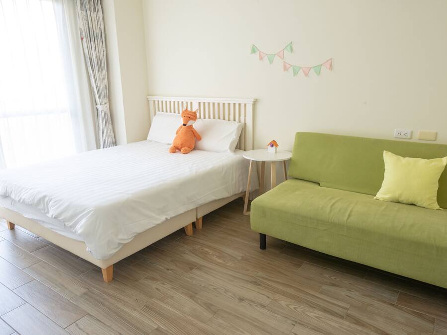 A bedroom with a bed, a green sofa, a small round table, and a wall-mounted decoration.