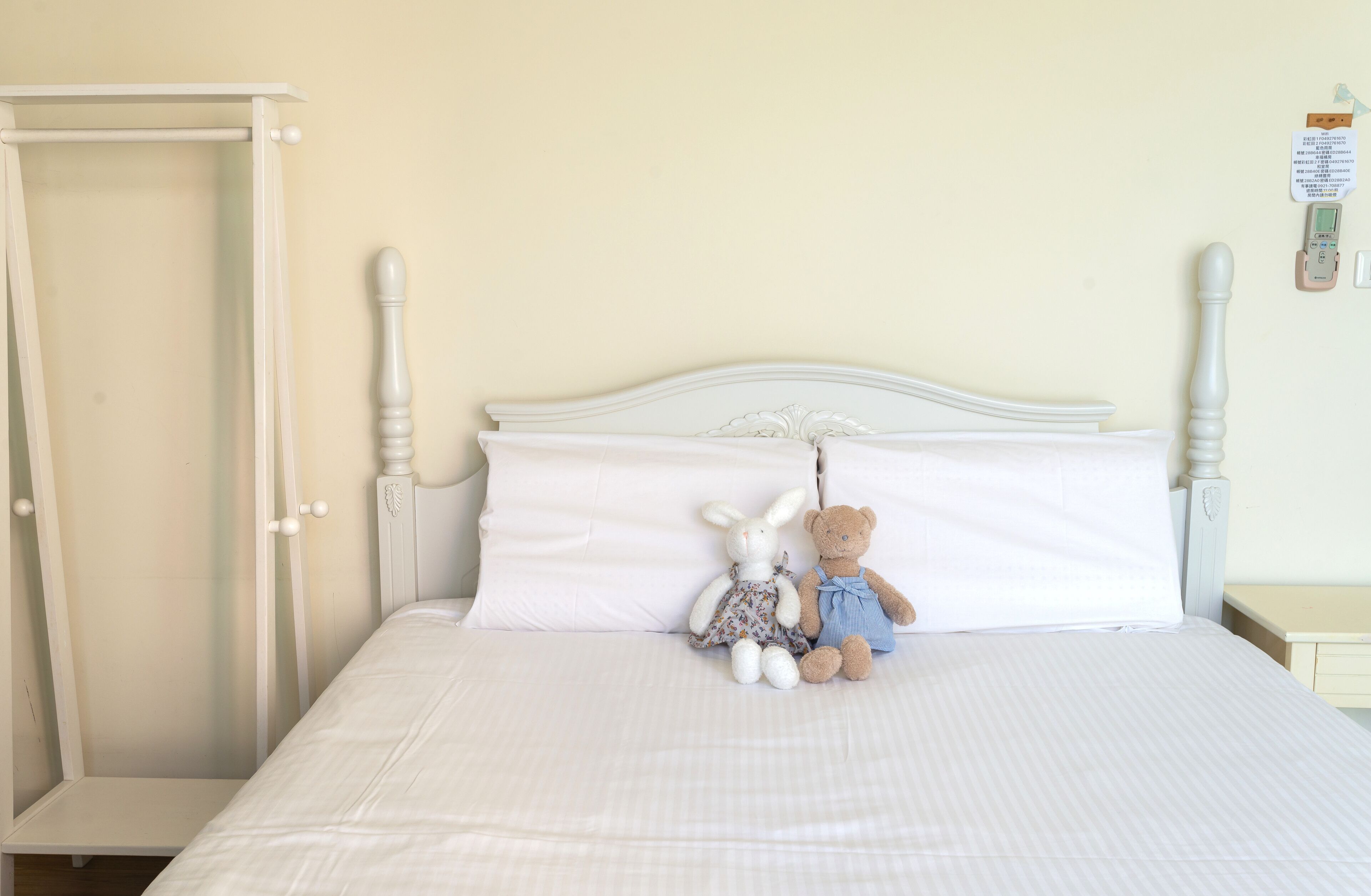 A bed with white bedding, a white headboard, and two stuffed animals on the bed.