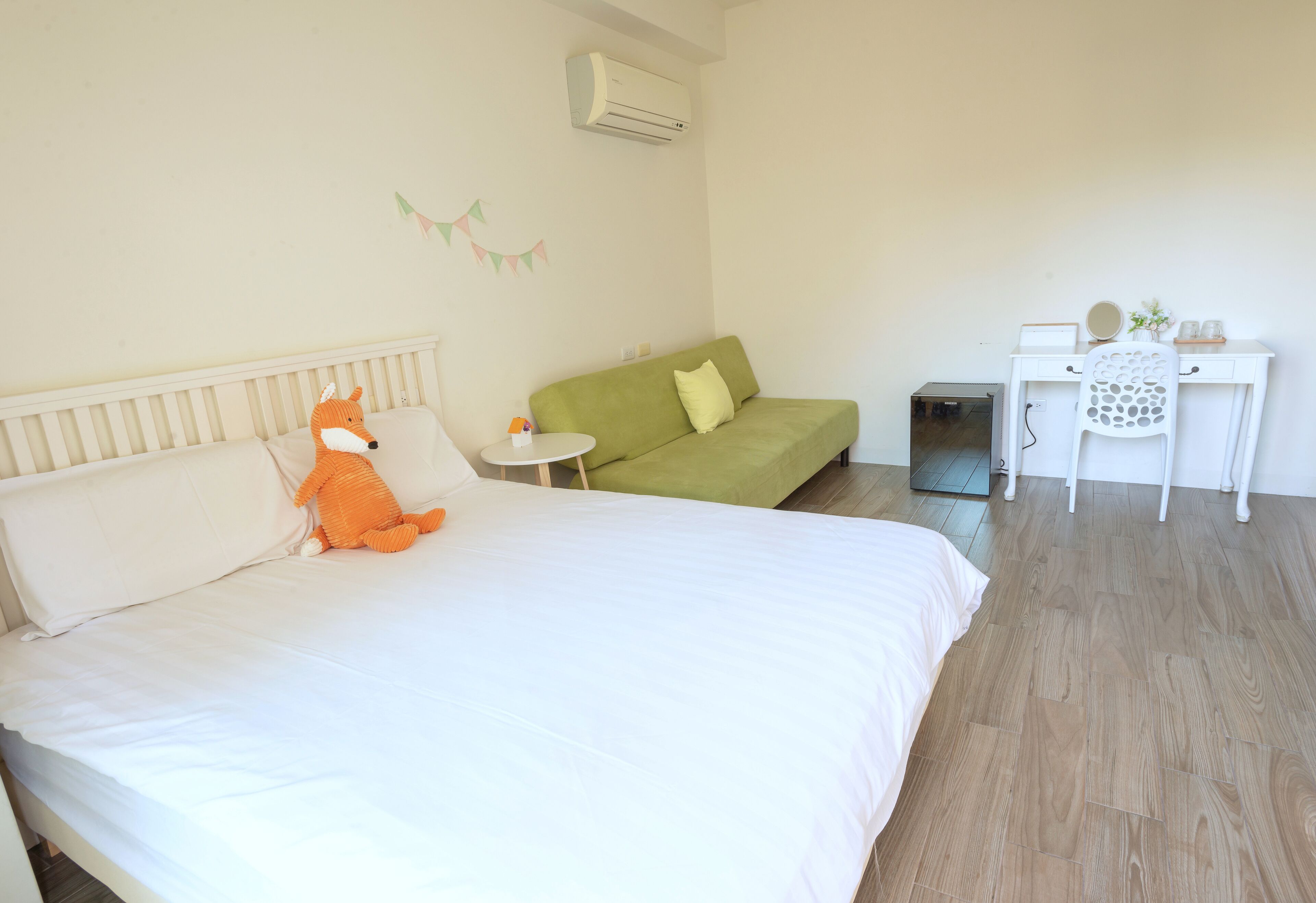 Une chambre à coucher avec un lit, un canapé vert, une petite table, un bureau blanc et un appareil de climatisation.