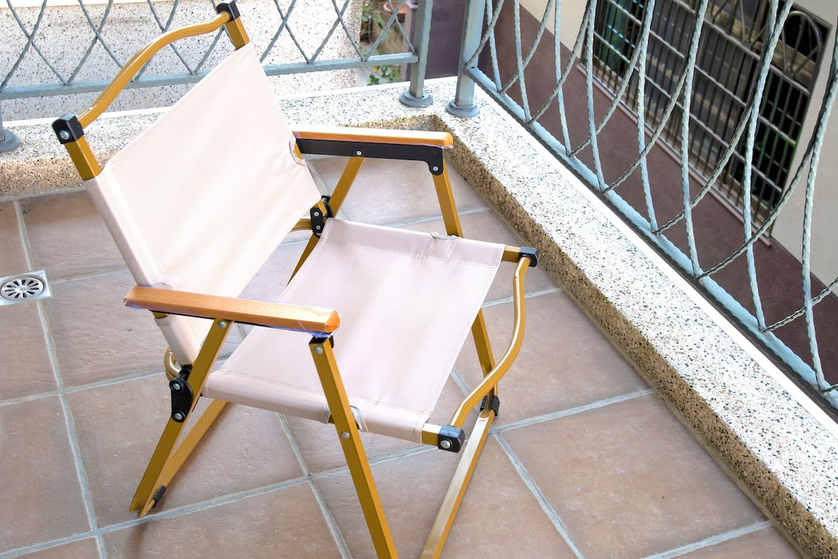 Una silla plegable en un balcón empedrado con barandillas de metal.