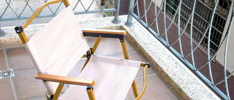 A foldable chair on a tiled balcony with metal railings.