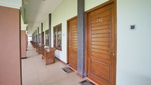 Un pasillo con puertas de madera numeradas 202 y 203, sillas de madera y un bote de basura.