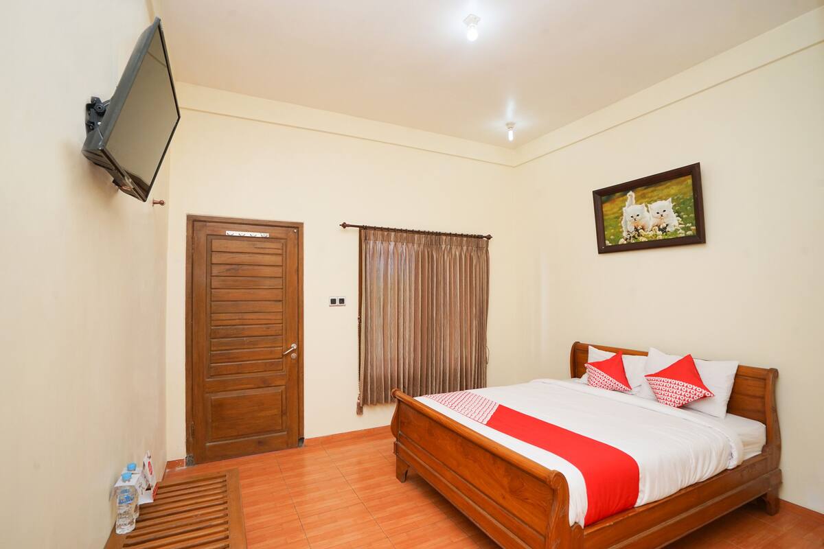 A bedroom with a wooden bed, a TV mounted on the wall, a door, and a window with curtains.