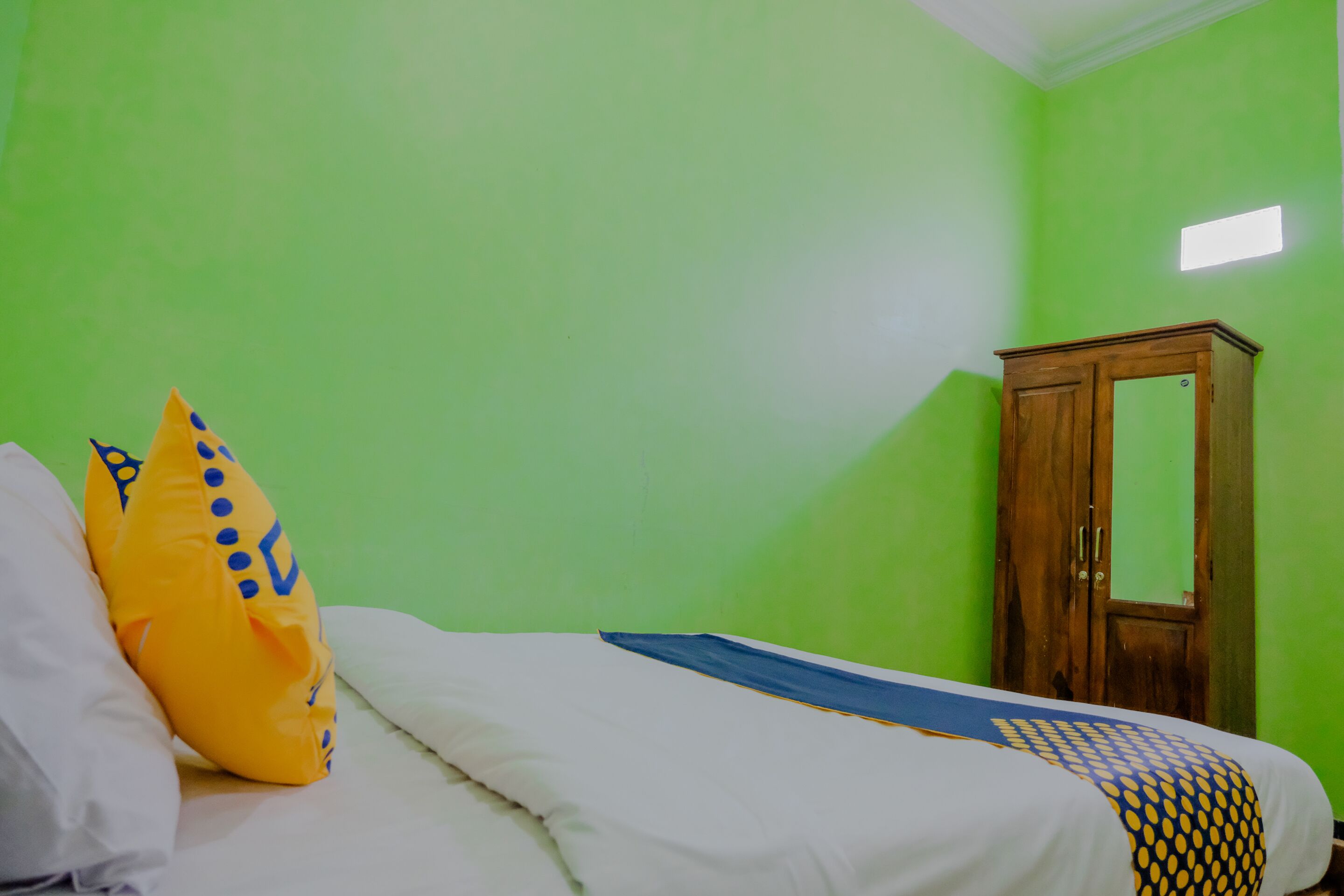 Una stanza con un letto, pareti verdi, un armadio in legno e una piccola finestra.
