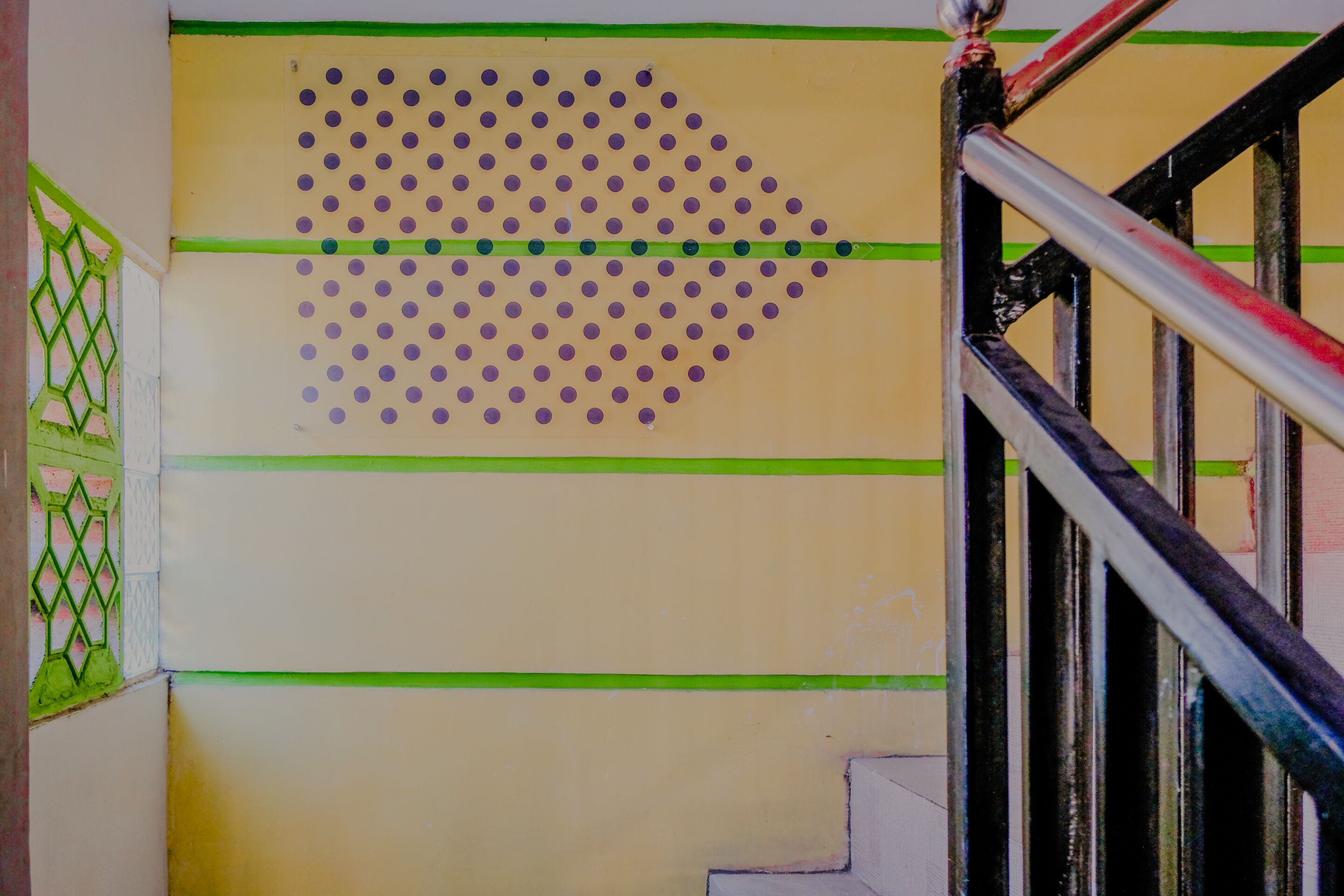 A staircase with a yellow wall featuring a large arrow pointing to the right, green horizontal lines, and a metal handrail.