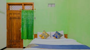 A bedroom with a wooden door, green curtains, a bed with patterned pillows, and a green wall.
