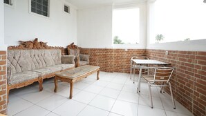 A room with a sofa, a coffee table, a dining table with chairs, and a brick wall. - OYO 2021 Wisma Vandera Syariah (Garut)