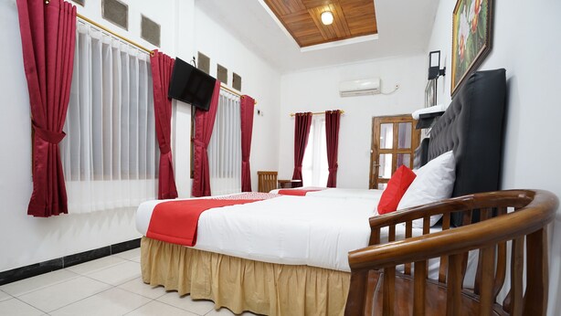 A neatly arranged bedroom with a bed, wooden headboard, and red curtains. - OYO 2021 Wisma Vandera Syariah (Garut)
