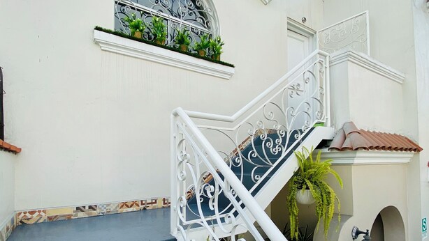 Un edificio blanco con una escalera azul y una barandilla metálica decorativa.