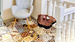 Una habitación con suelo de baldosas estampadas, un sillón capitonado y una barandilla blanca.