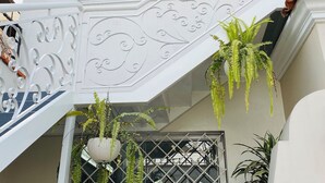 Un edificio blanco con una escalera decorativa, una ventana con reja de metal y plantas colgantes.