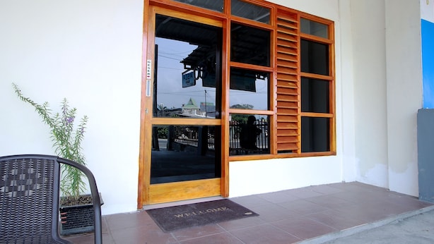 A building entrance with a large glass door and wooden shutters, a black chair, and a potted plant. - OYO 1335 Anie 71 Residence (Bengkulu)